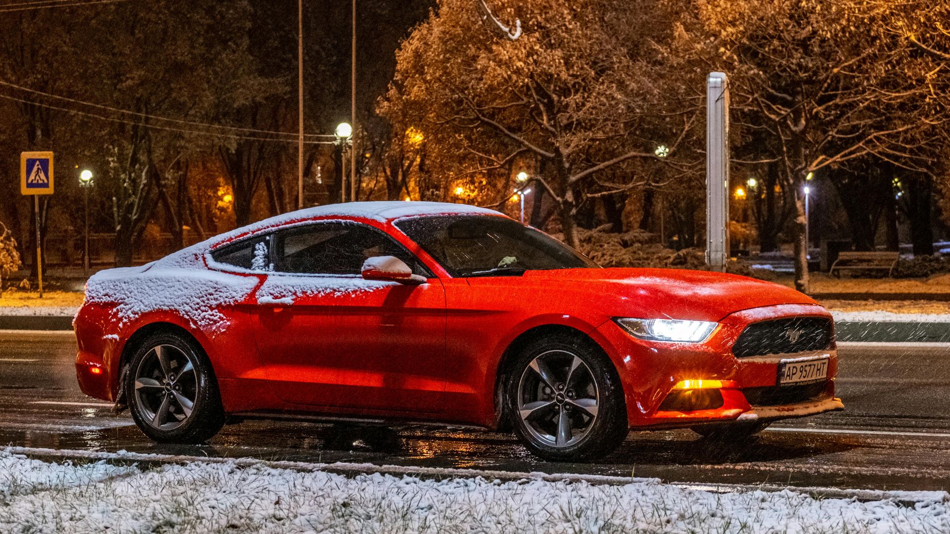 A vibrant red car parked on a snow-covered road at night, surrounded by winter scenery.