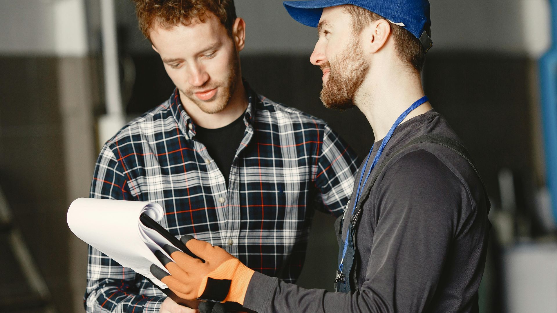 Mechanic in uniform consults with customer in garage setting beside a blue truck.