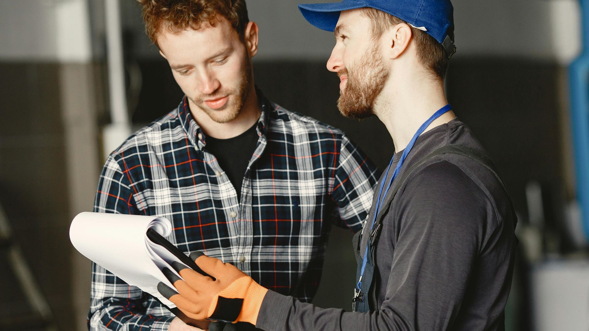 Mechanic in uniform consults with customer in garage setting beside a blue truck.