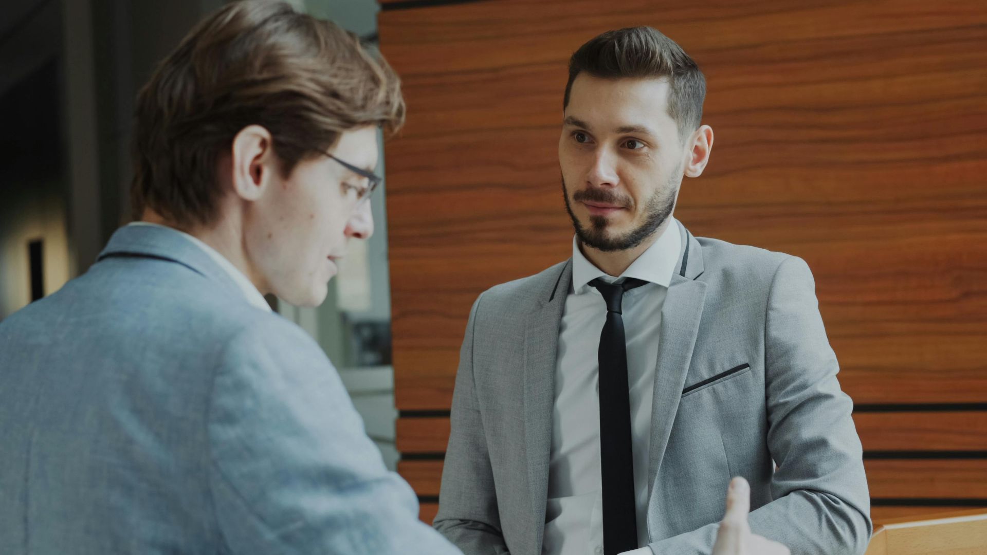 Two male professionals engaged in conversation in a modern office setting.