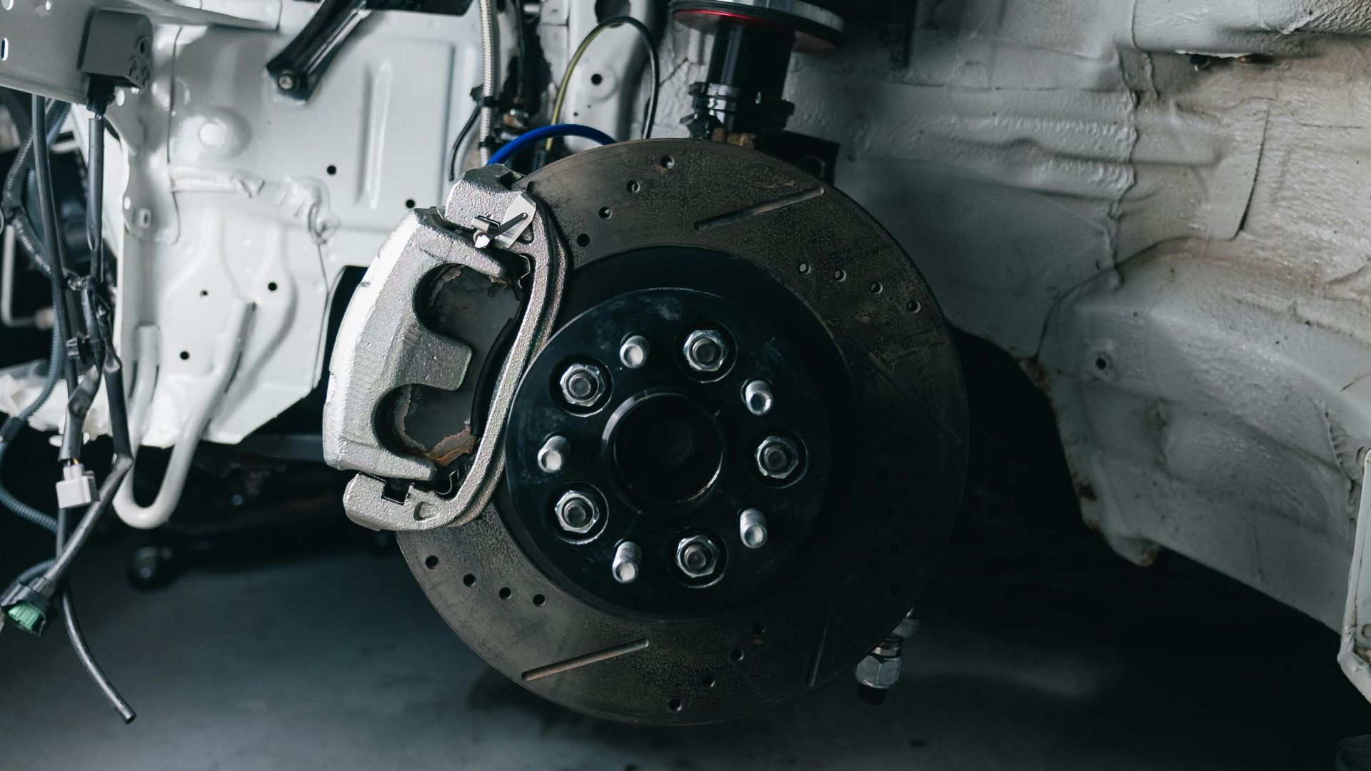 Close-up shot of a vehicle's suspension and brake assembly in a garage setting.
