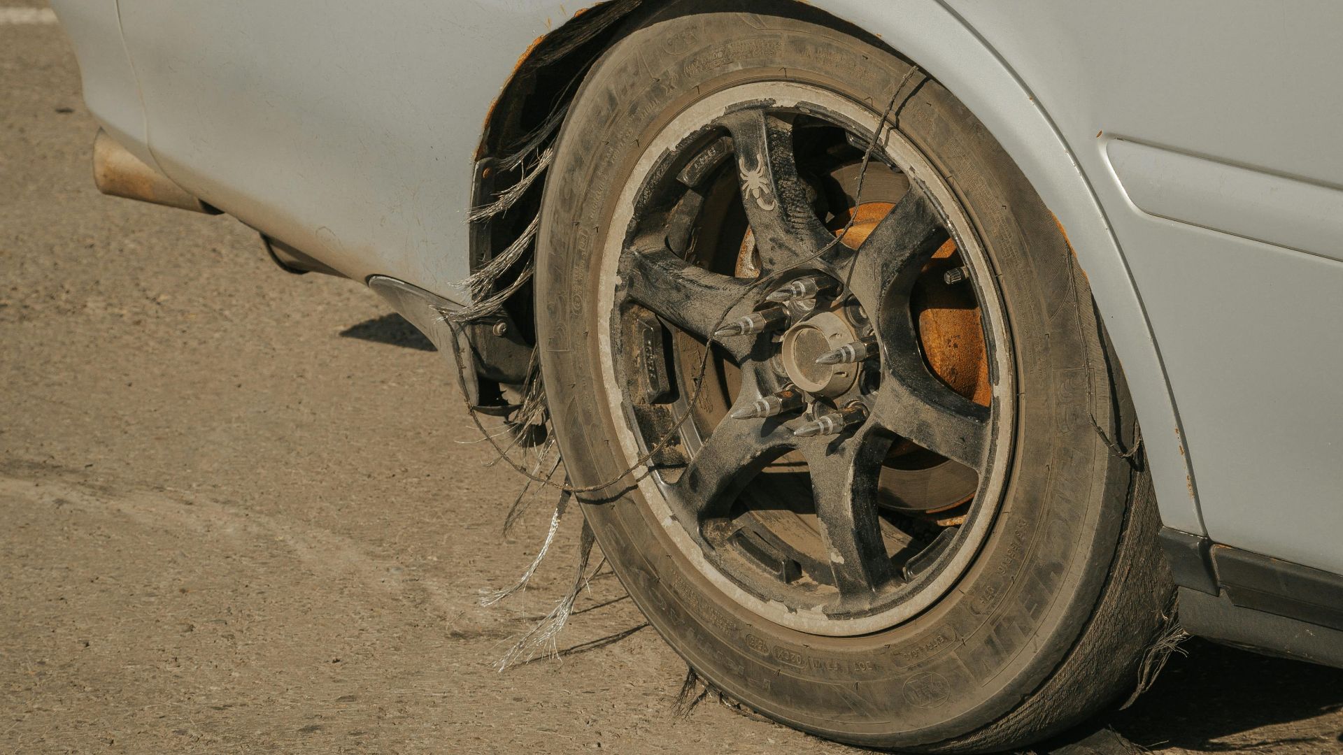 Close-up of a blue car with a severely damaged tire on weathered concrete.