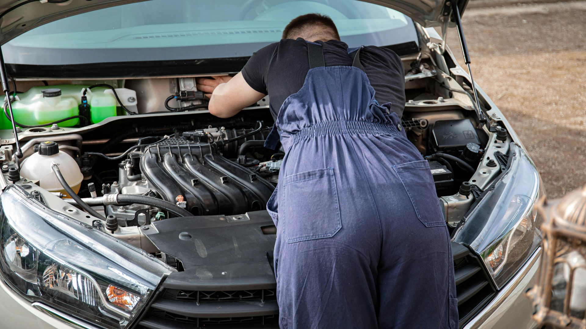 An automotive mechanic performing engine maintenance on a car outdoors, showcasing mechanical skills.