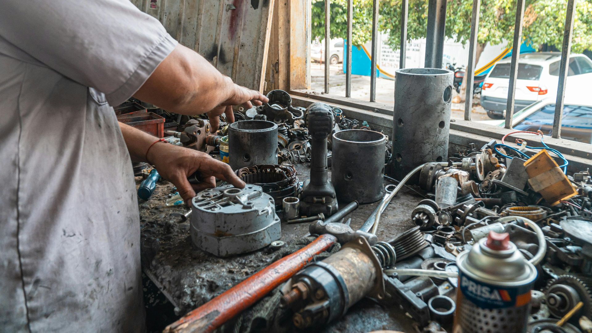 Mechanic arranging car parts on a cluttered work table in an automotive workshop.