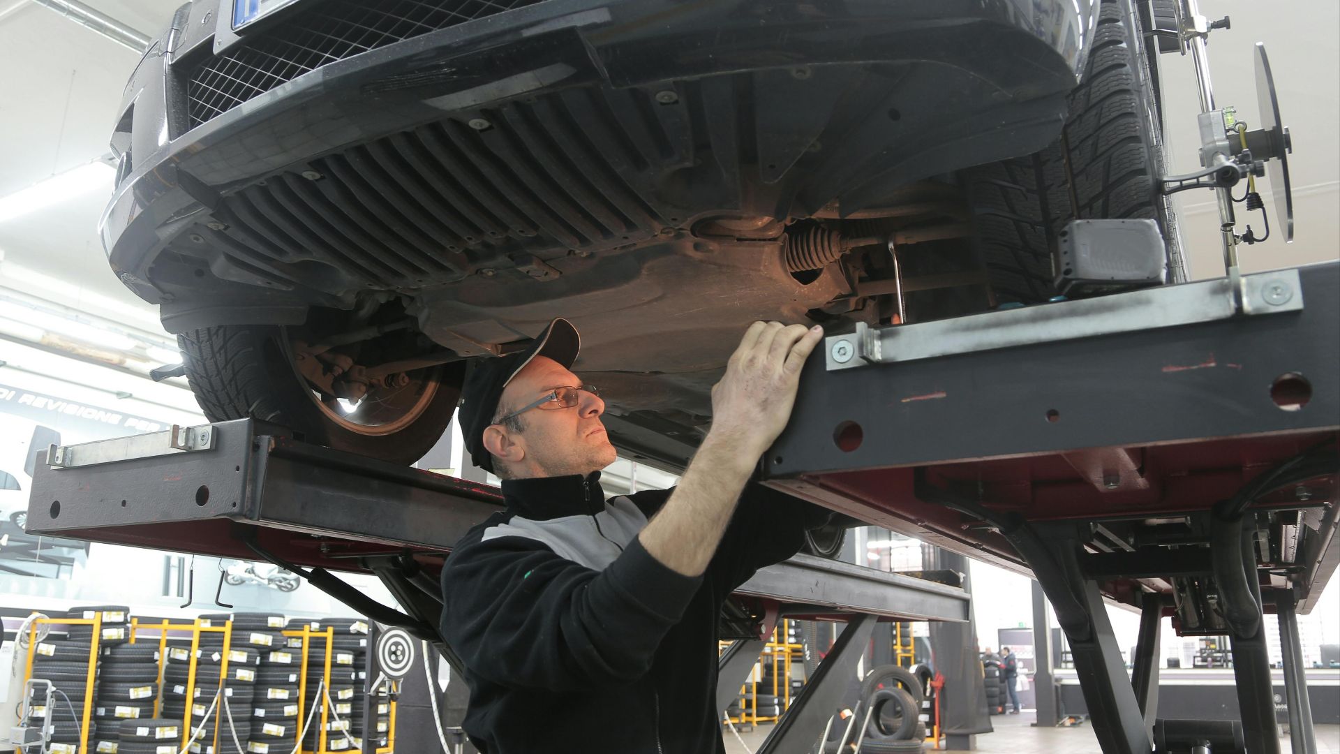 Mechanic inspecting car on lift in an automotive garage, focusing on vehicle repair and maintenance.