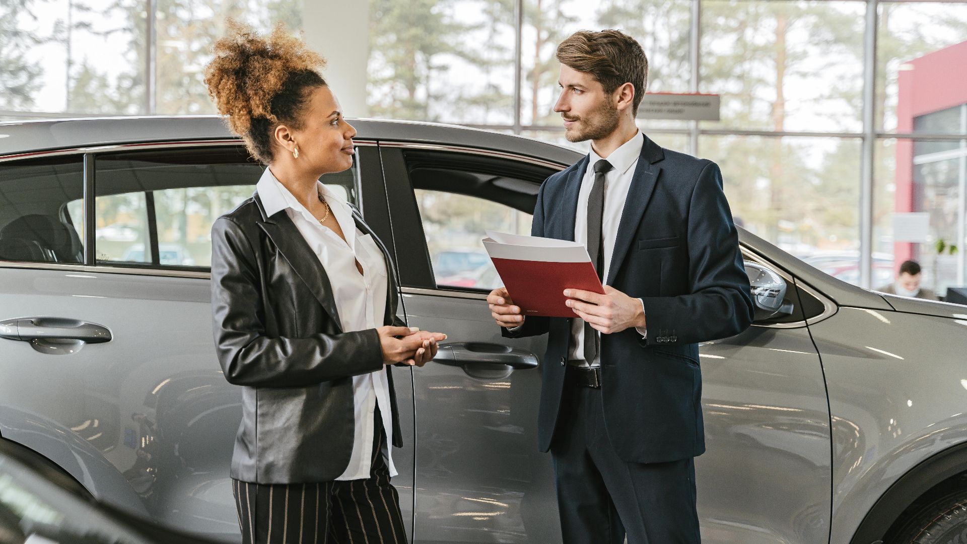 A woman discussing car purchase with a dealer inside a car dealership showroom.