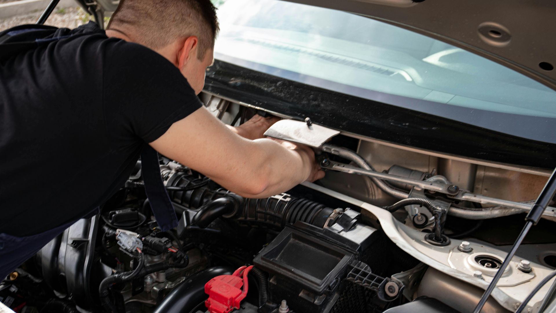 A mechanic busy repairing an engine under the hood of a car in a garage setting.
