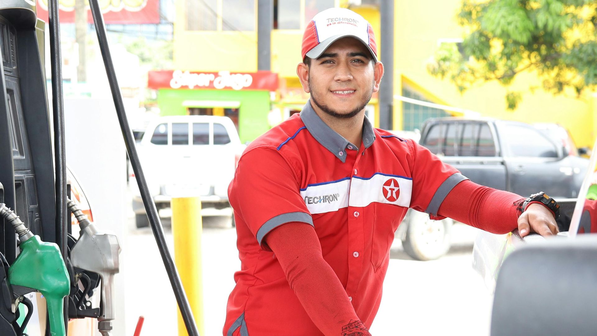Cheerful gas station attendant refueling a car during the day.