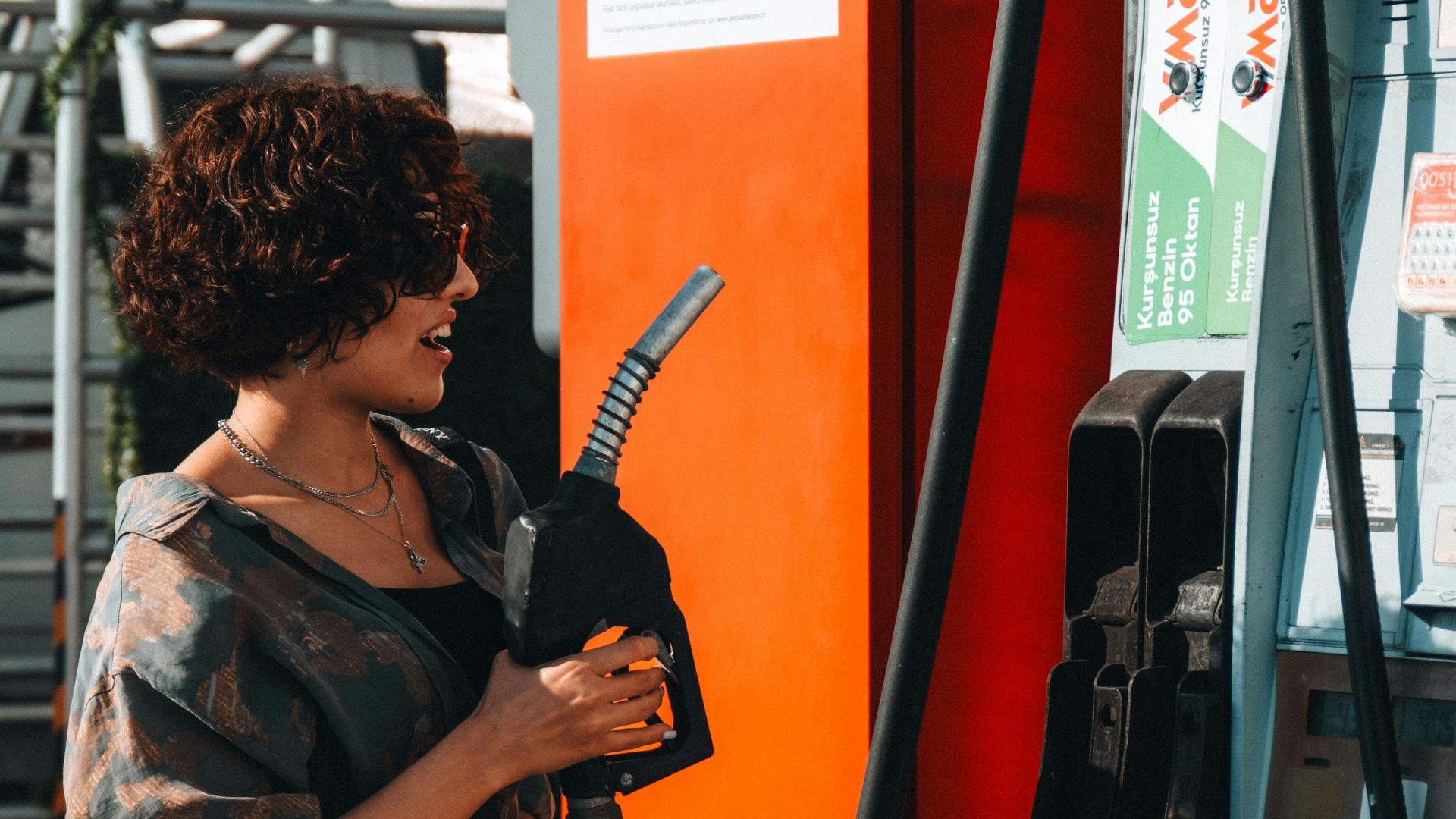 Woman refueling her car at a modern gas station during the day, under bright sunlight.