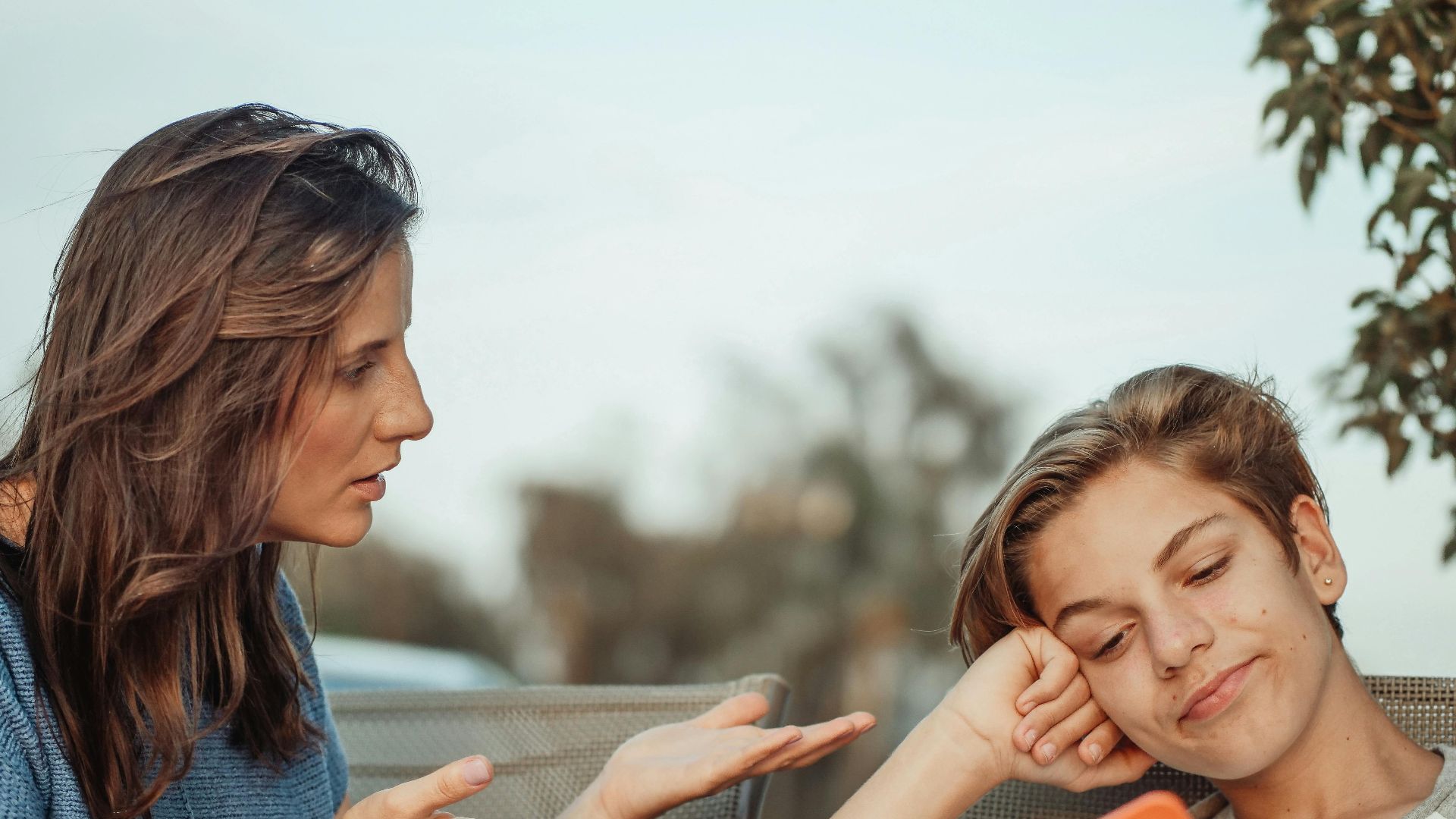 A mother engaging with her teenage son holding a smartphone outdoors.