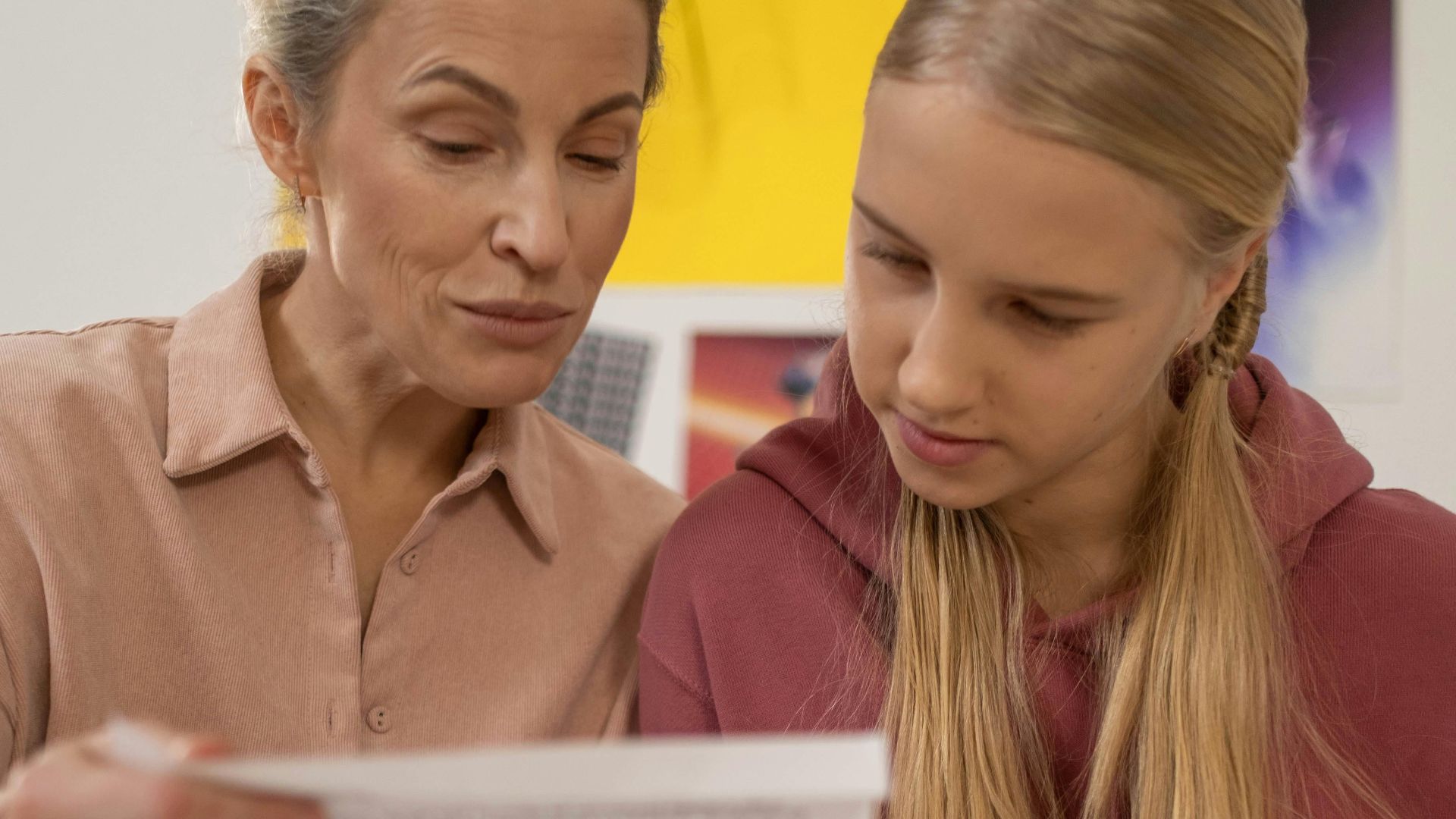 A mother and teenage daughter reading papers attentively at home.