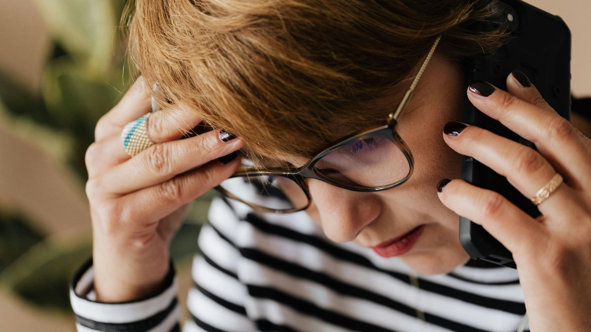 Focused woman with eyeglasses discussing work over a phone call, looking concerned and thoughtful.