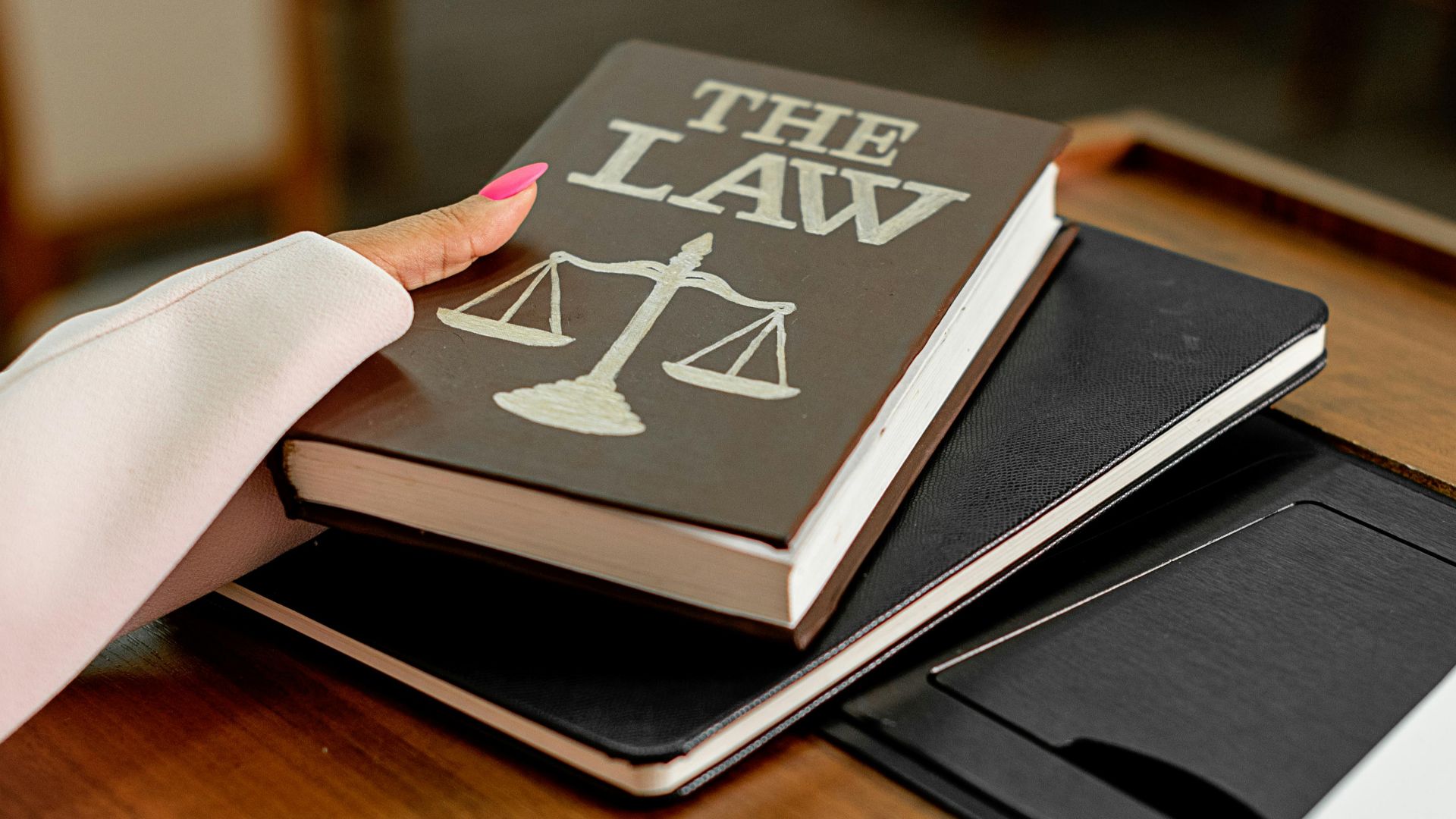 Closeup image of a law book titled 'The Law' on a wooden desk with scales of justice.
