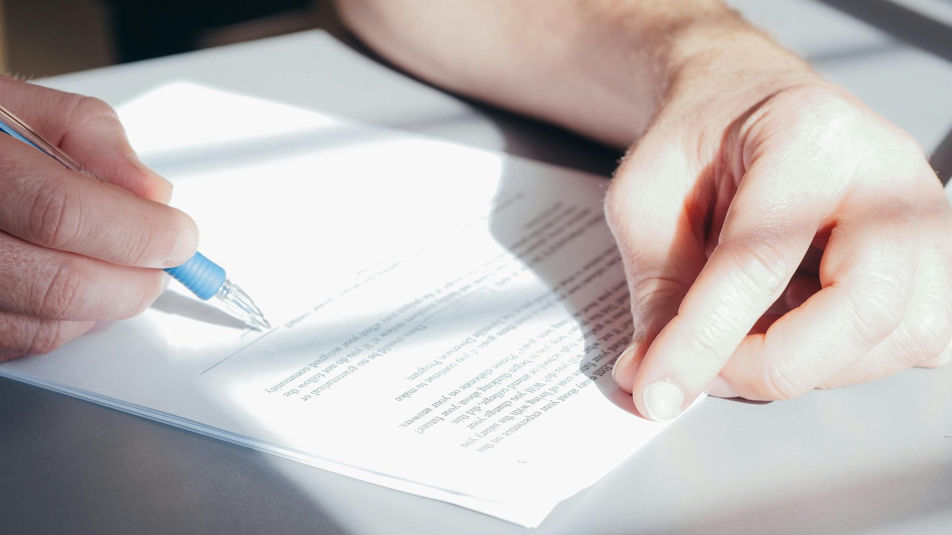 Hands signing a contract with a blue pen, close-up view.
