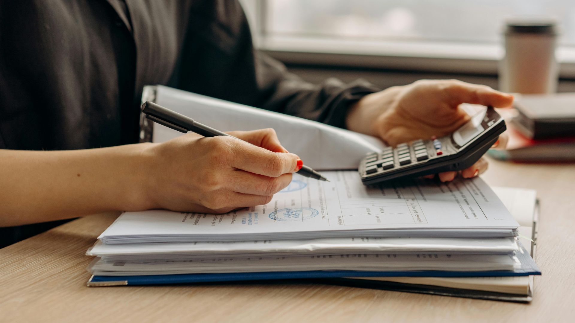 Close-up of person using a calculator with financial documents in an office.