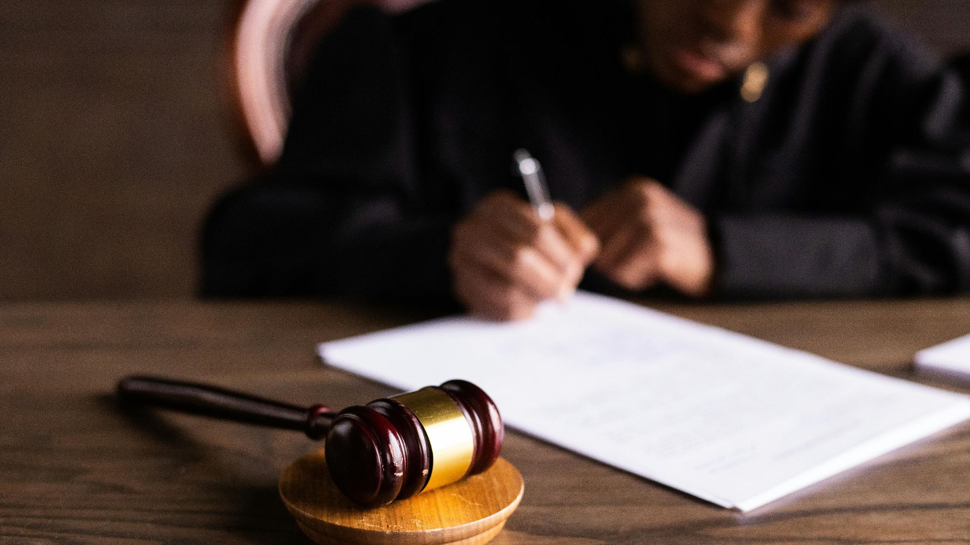 Judge signing documents at desk with focus on gavel, representing law and justice.