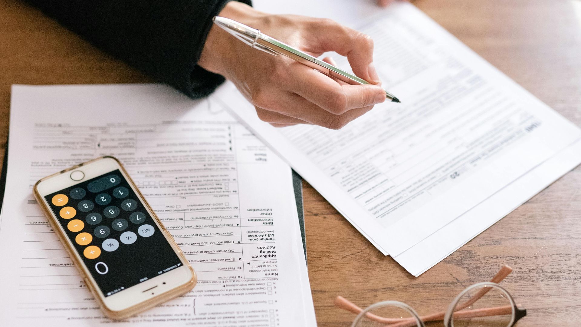 A woman reviewing financial documents with a calculator and glasses on a table.