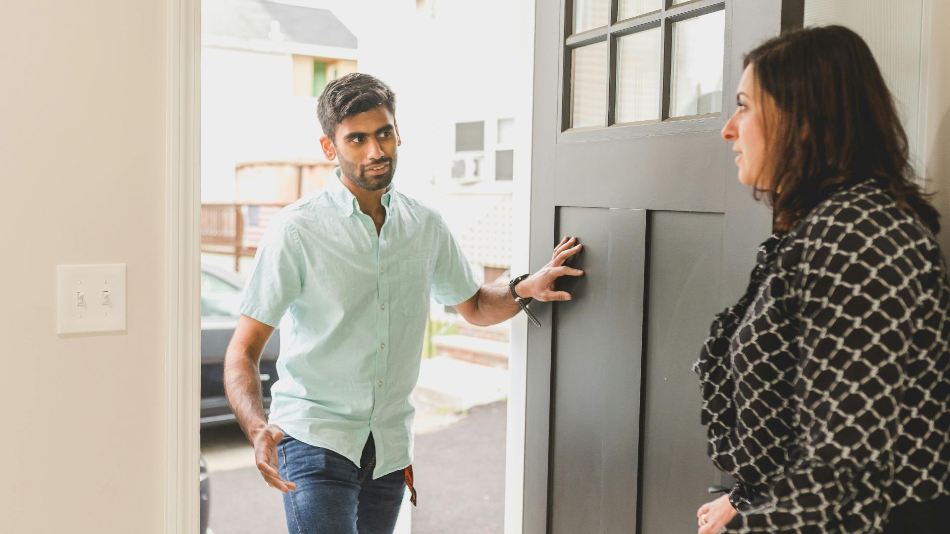 A man enters a home, conversing with a woman standing nearby in a casual setting.