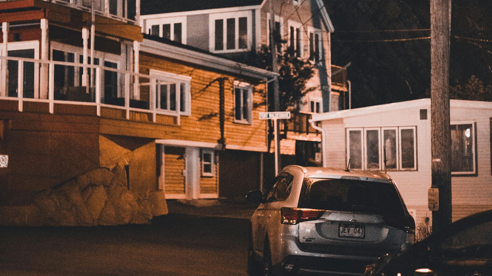 Dramatic night view of residential houses and parked cars under a glowing streetlight.