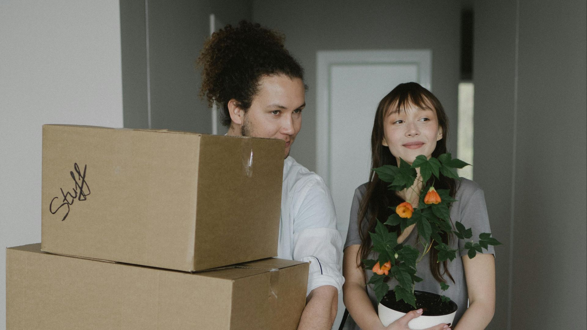 A young couple carrying boxes and a plant into their new home, symbolizing a fresh start.