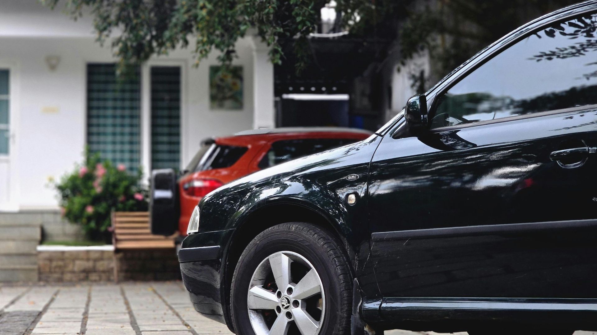Close-up view of cars parked in a driveway with a modern house in the background.