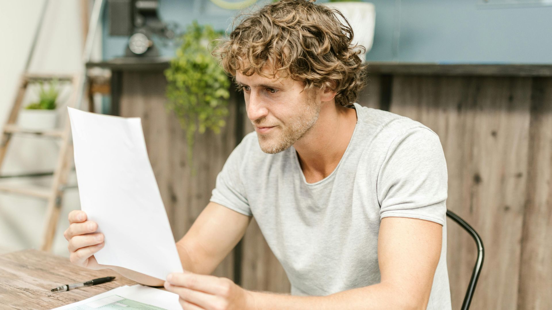 A man with curly hair evaluates documents at a desk, highlighting focused work in a professional setting.