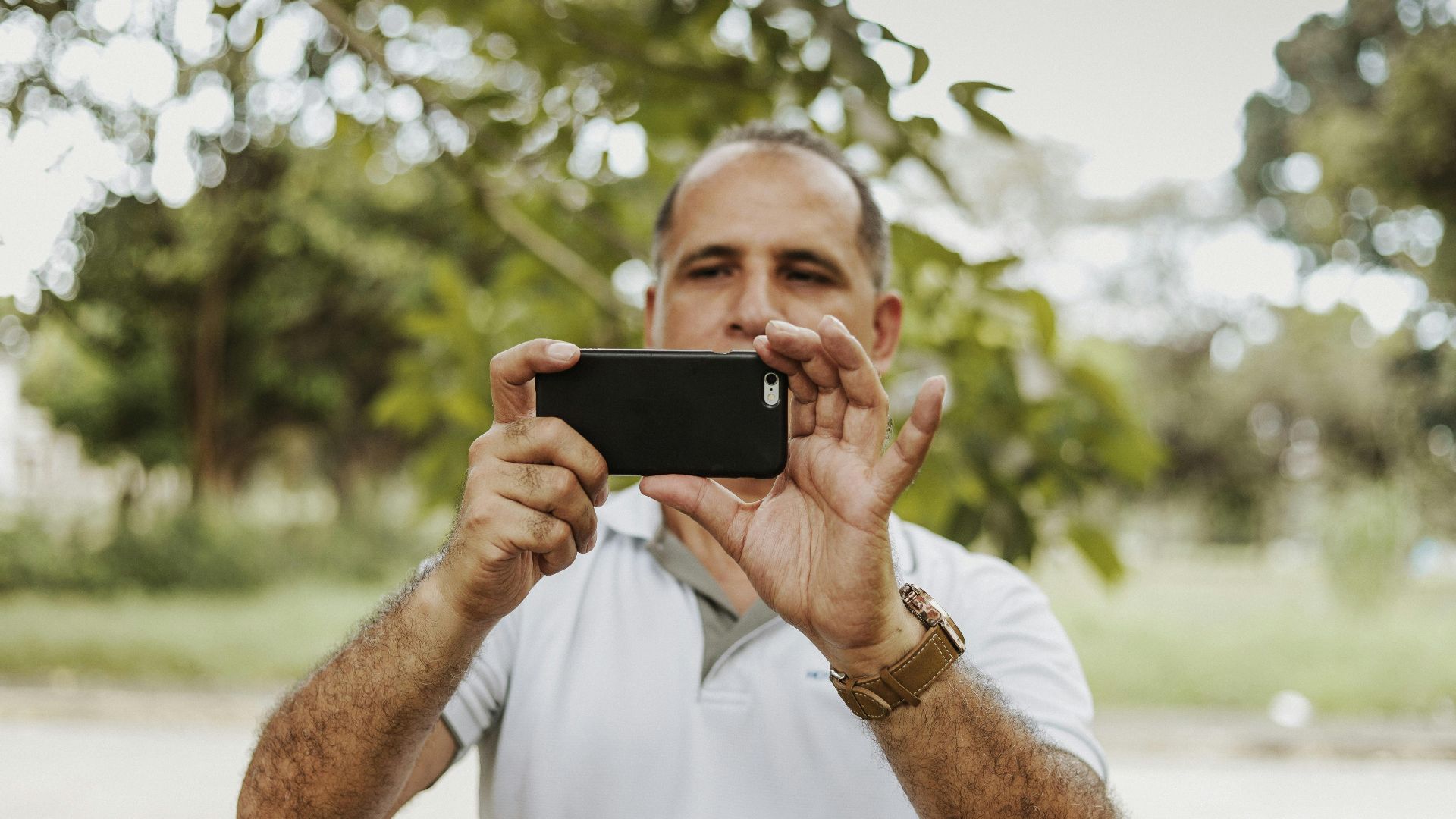 Adult man using smartphone to take a photo in a natural setting, showcasing modern technology and leisure.