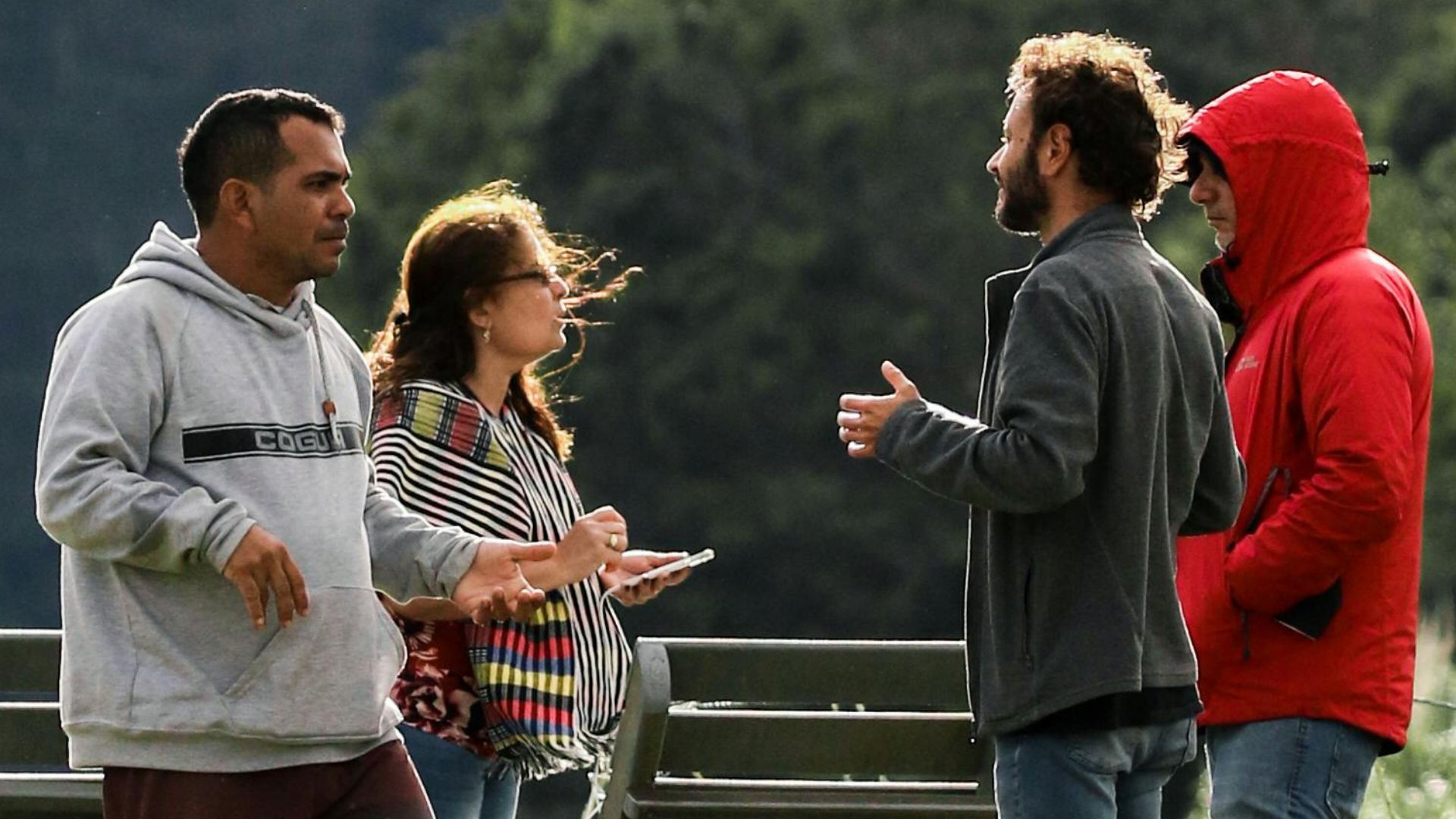 People conversing by a lake with a scenic mountain backdrop and a branded flag.