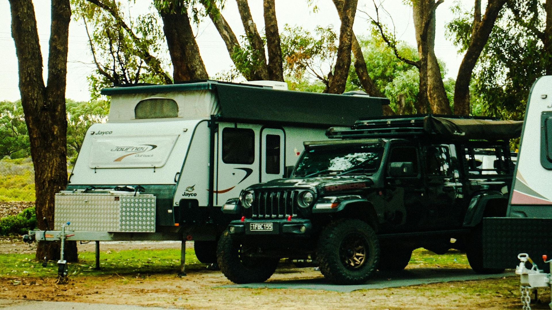 A camper and a Jeep parked in a serene forest environment, ideal for outdoor adventures.