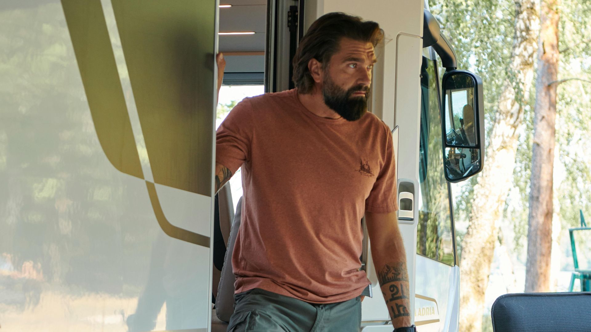 Bearded man stepping out of camper van in sunny Lithuania, showcasing outdoor adventure.