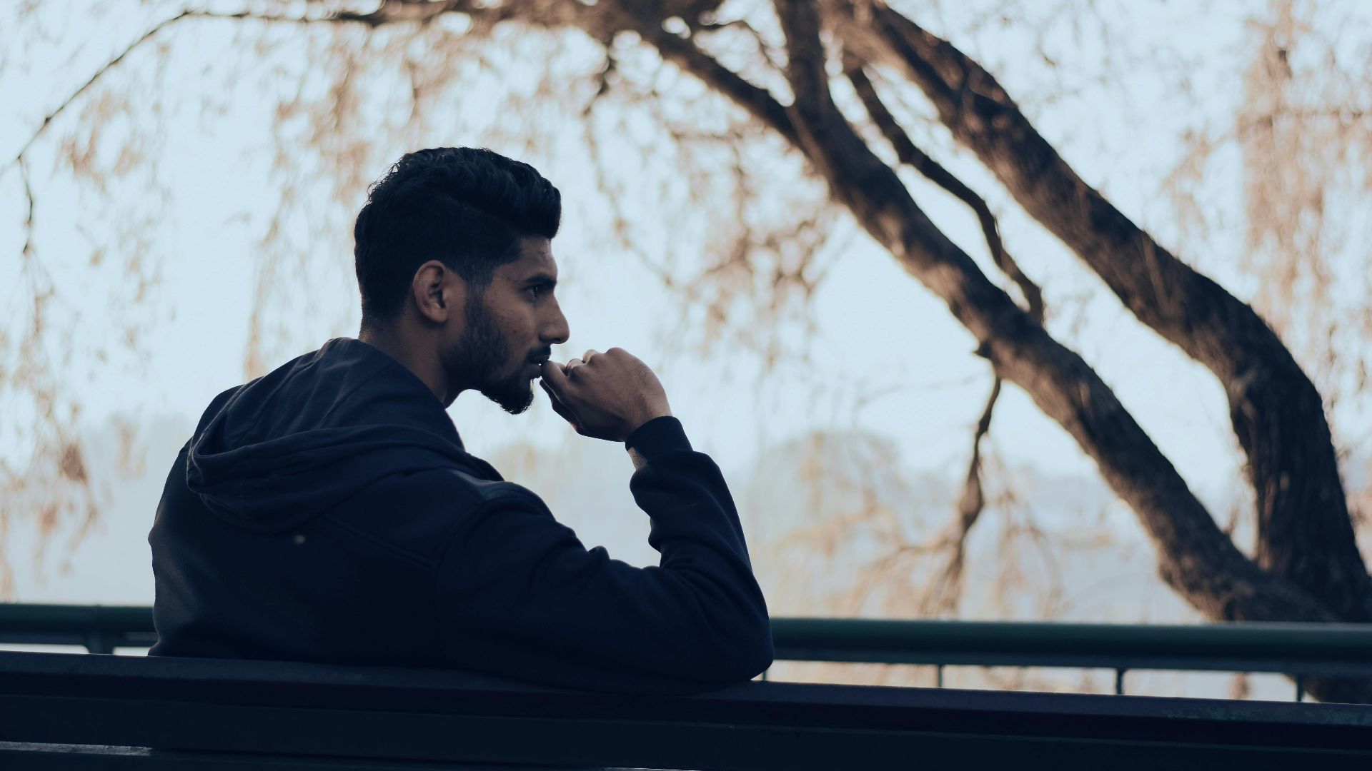 Man in deep thought sitting on a bench in a serene autumn park setting.