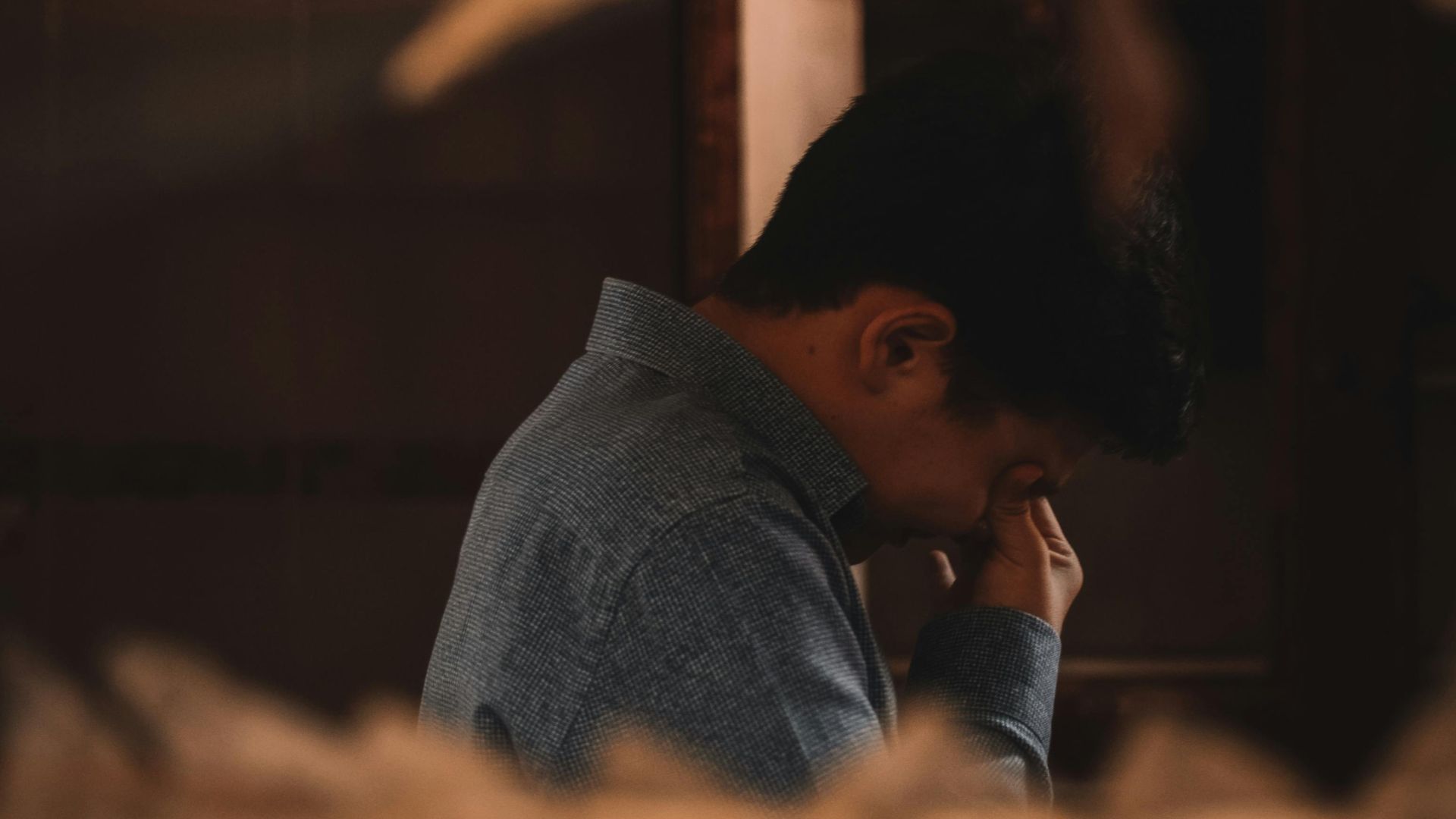 A man in deep thought captured indoors through a broken wall.