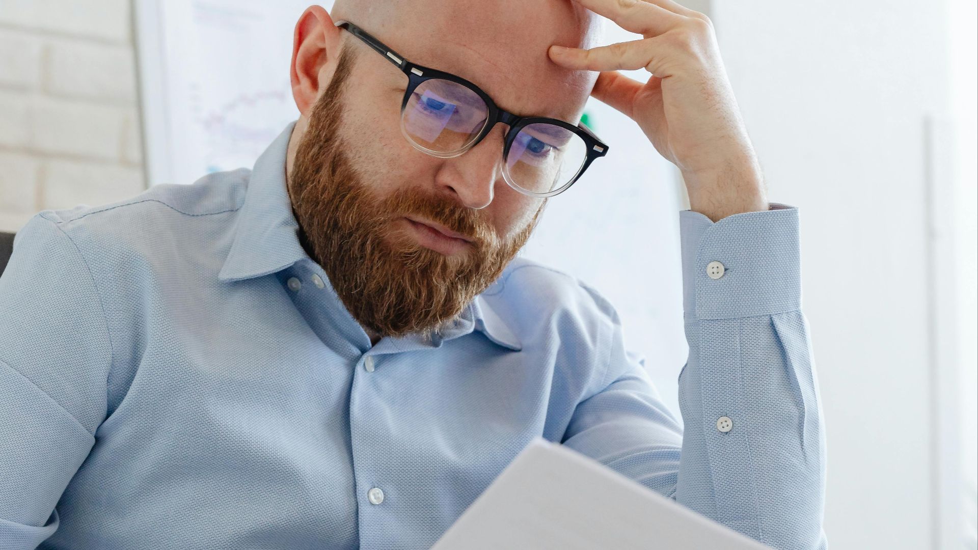 Caucasian businessman with beard and glasses reviewing documents in a modern office setting.