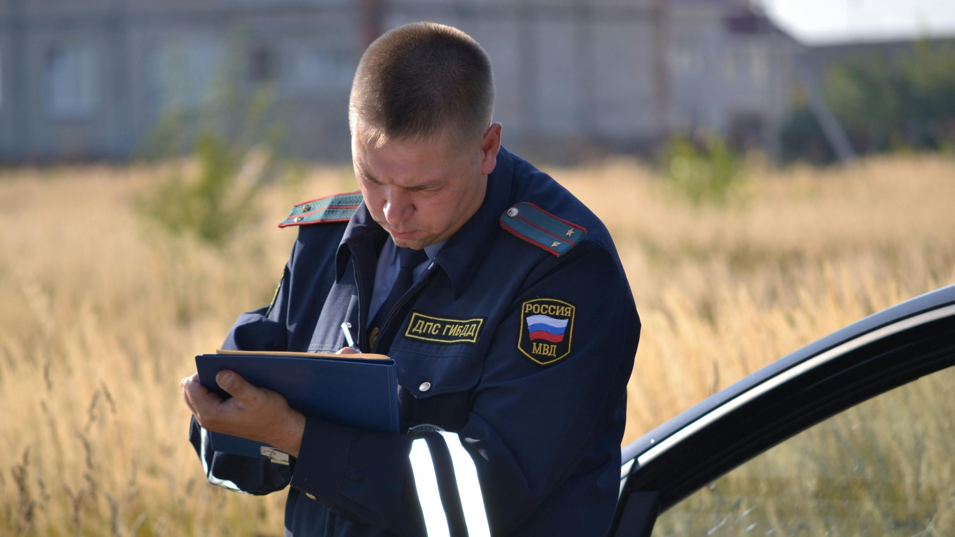 Police officer in uniform taking notes beside a car in a field.