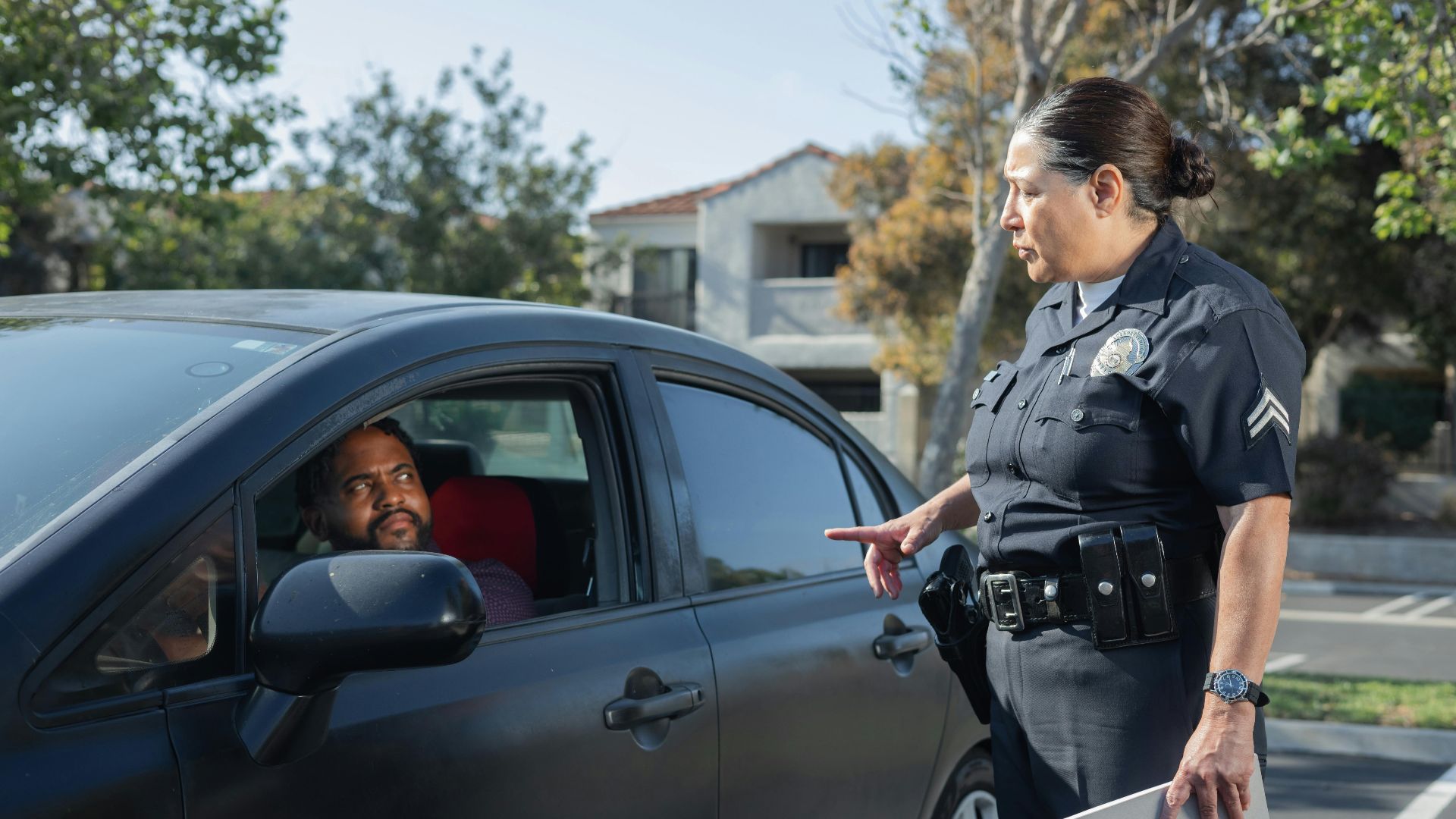 A police officer interacts with a driver during a daytime traffic stop on a residential street.