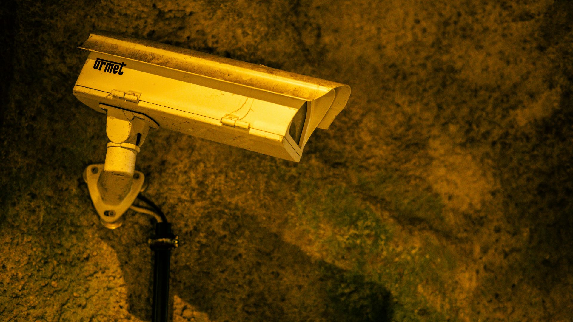 Close-up of a security camera mounted on a textured wall at night.