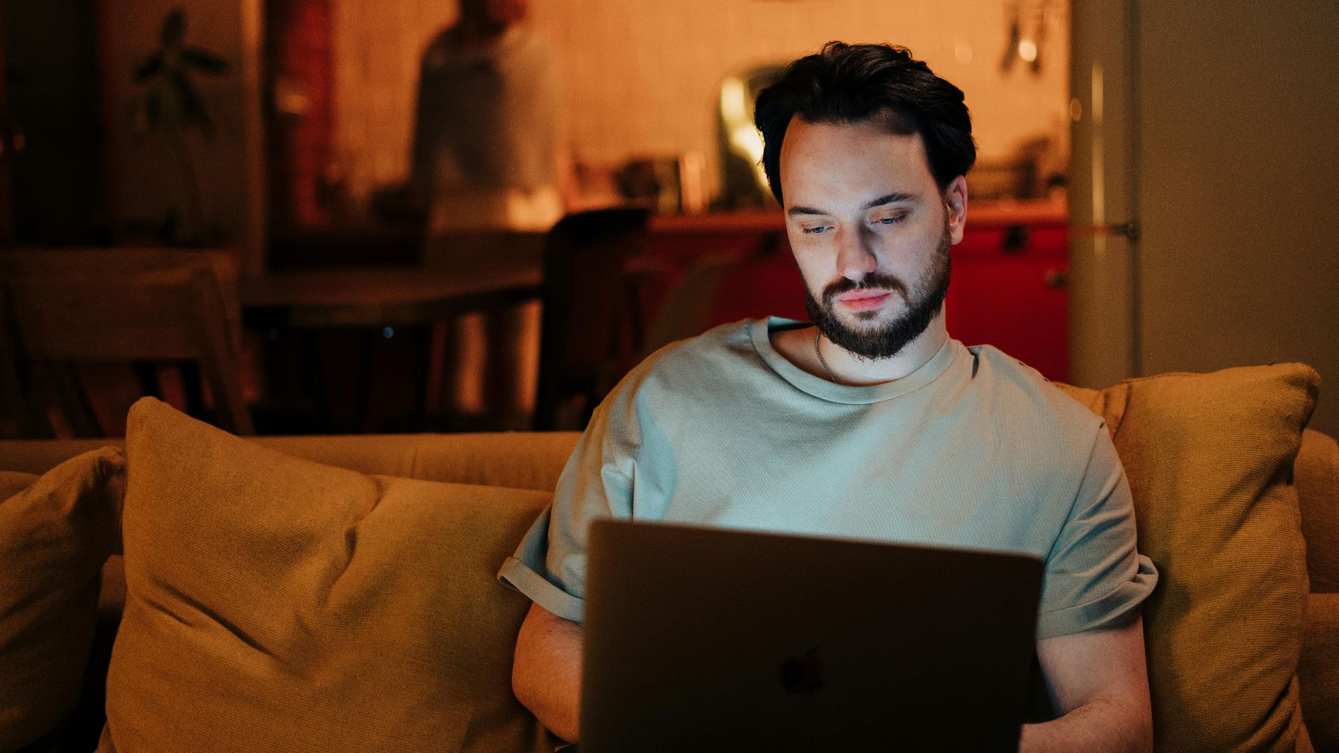 Man working on laptop at home, cozy evening atmosphere with warm light.