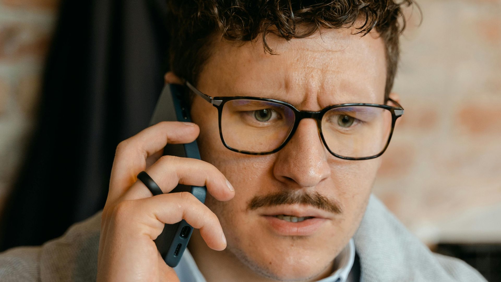 A man with curly hair and glasses engaged in a phone conversation indoors.