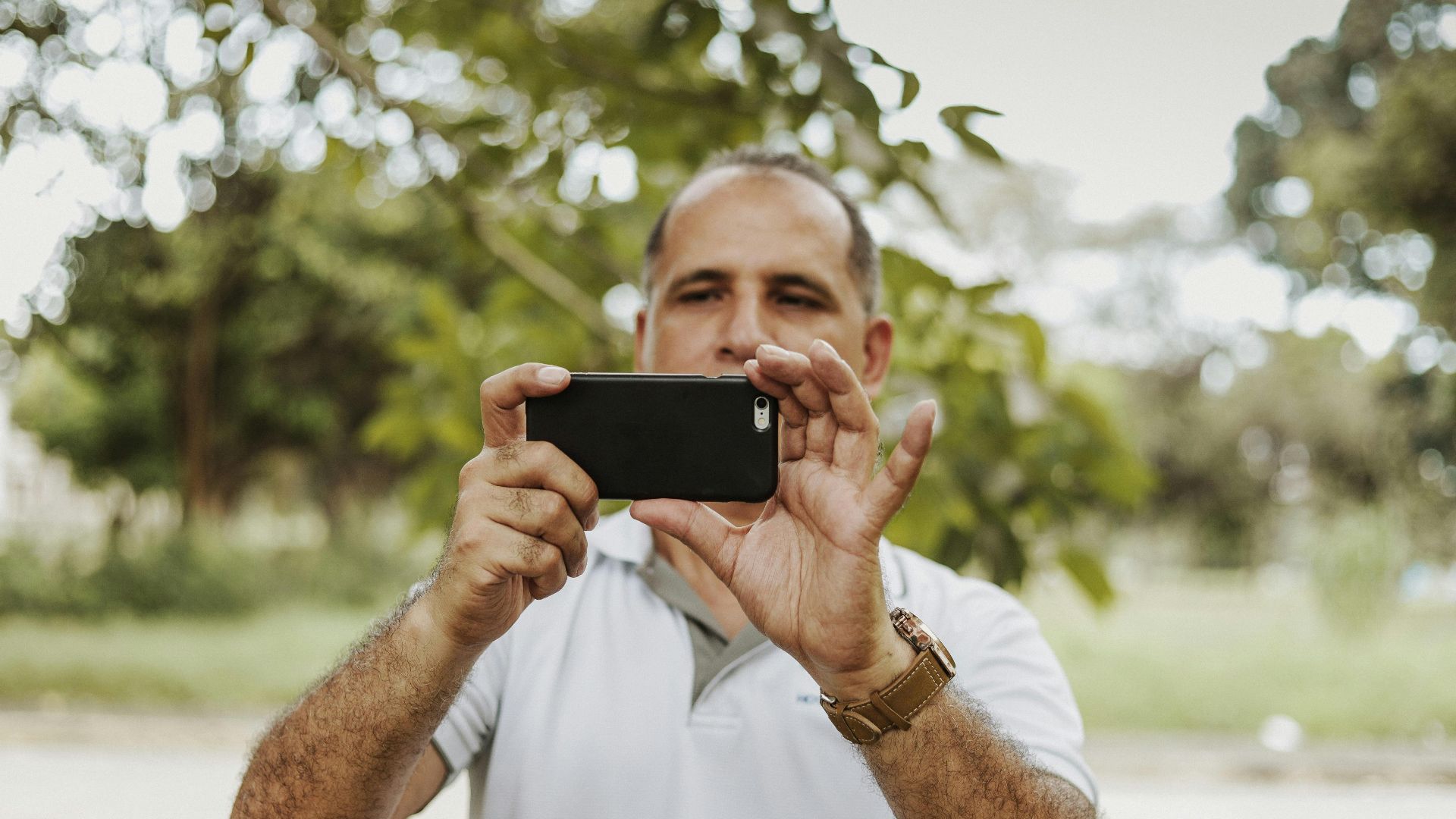 Adult man using smartphone to take a photo in a natural setting, showcasing modern technology and leisure.