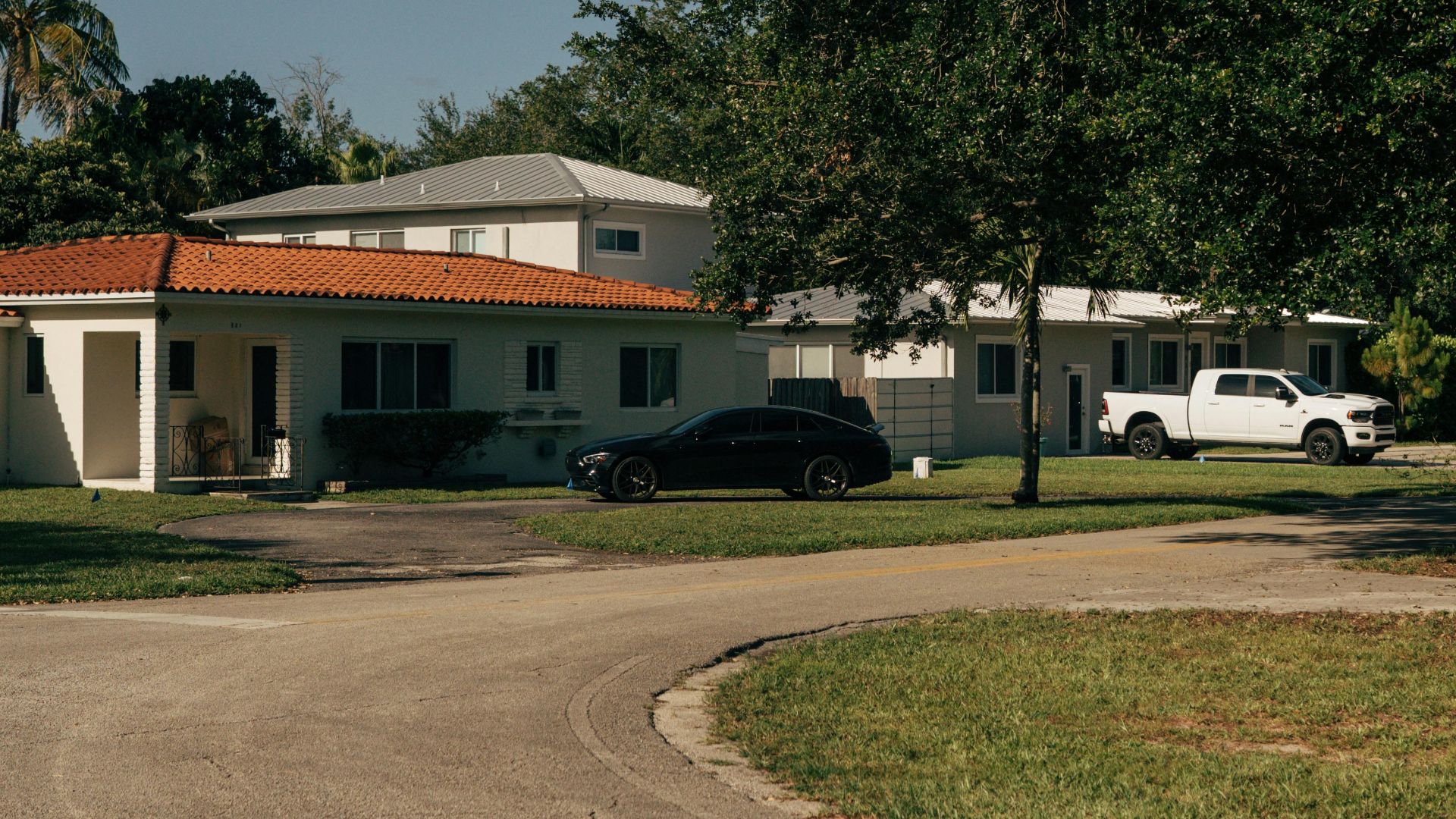 Peaceful suburban street with houses, trees, and cars under a clear sky.