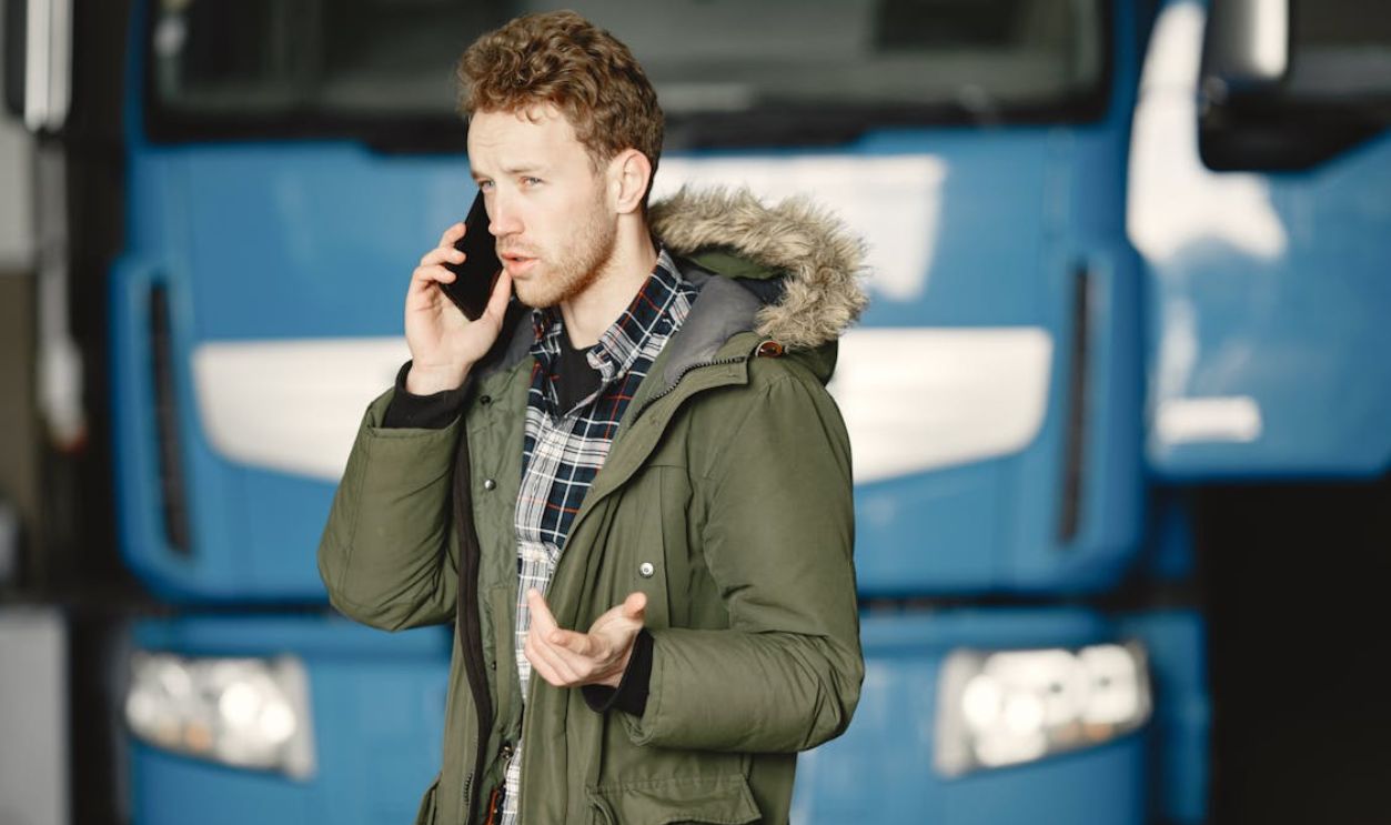 Man in Green Coat Talking on the Mobile Phone Beside Blue Truck
