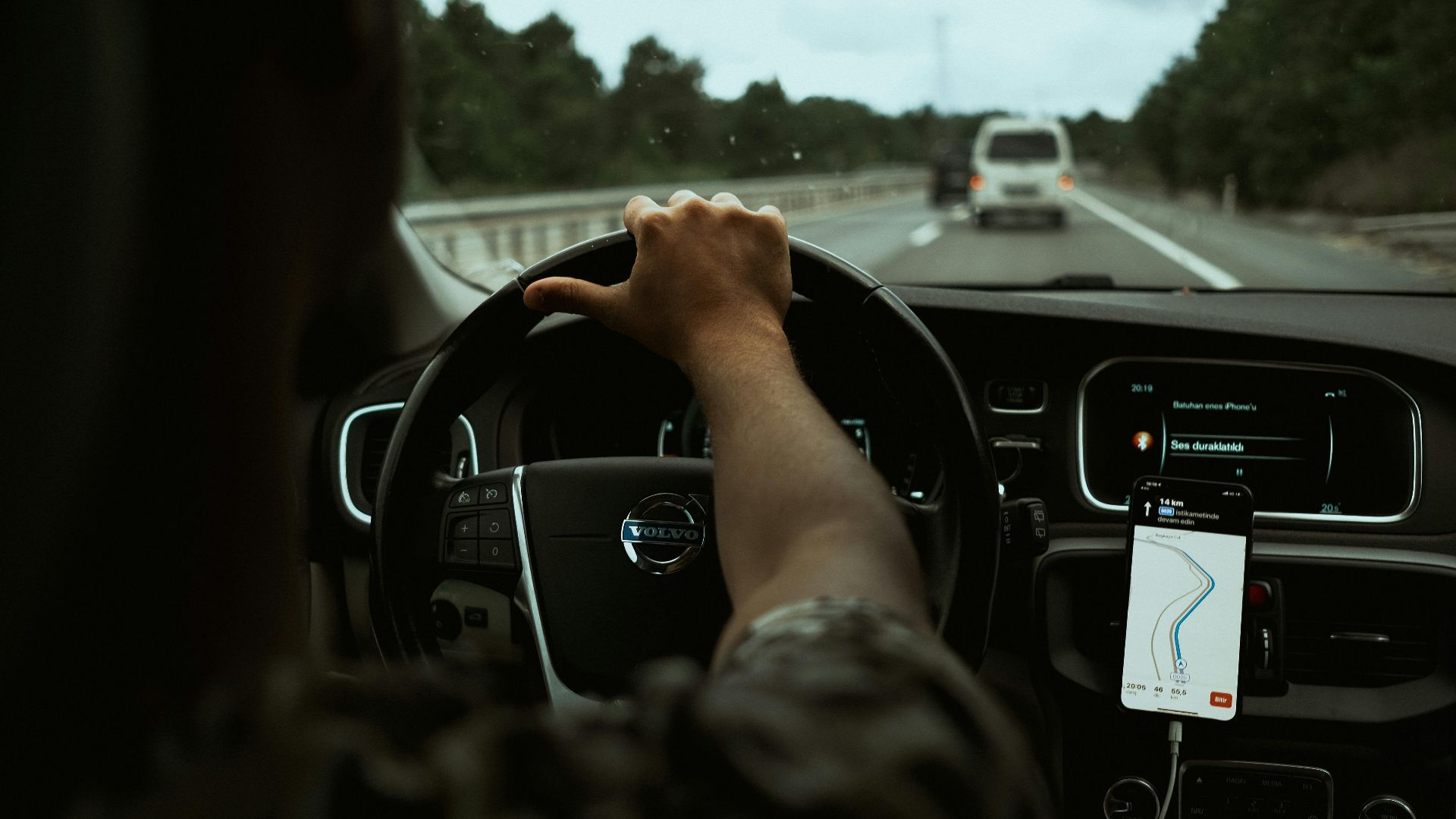 A driver navigates the highway with a smartphone GPS, showcasing modern car interior design.