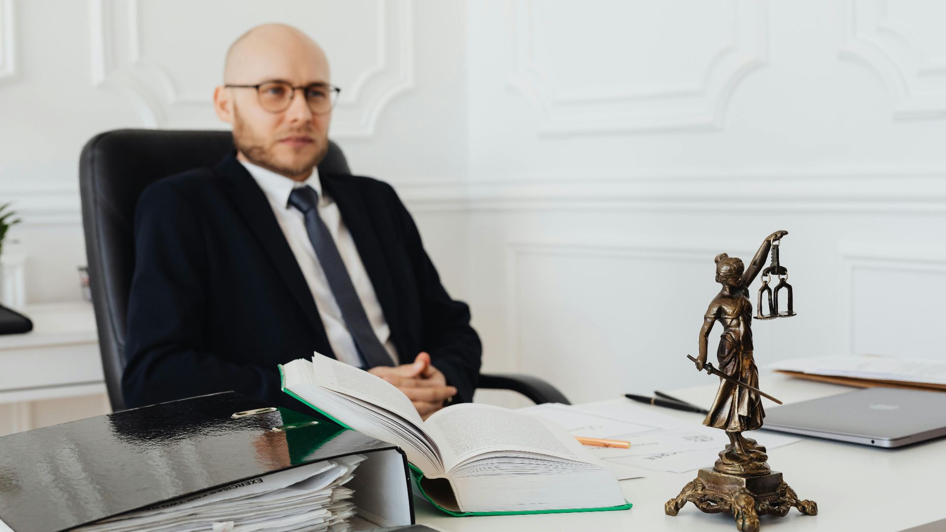 Bald lawyer in office sitting with legal documents and Justice statue.