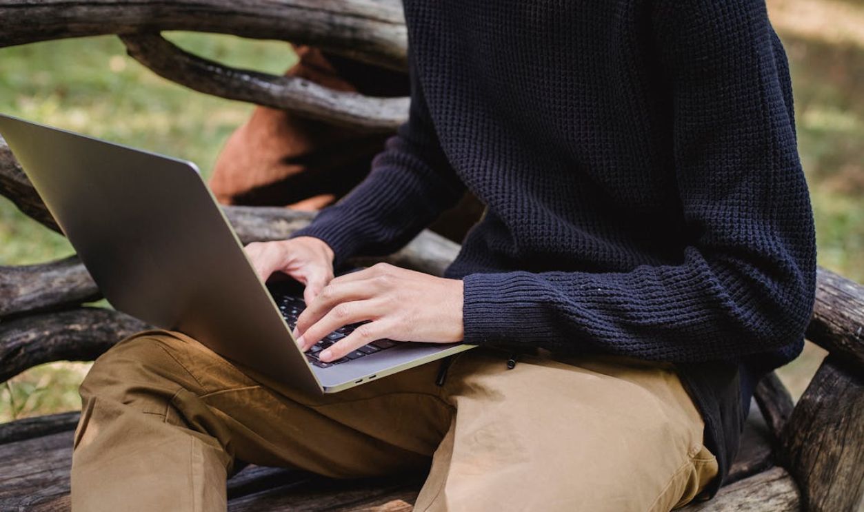 Crop unrecognizable man typing on laptop in park