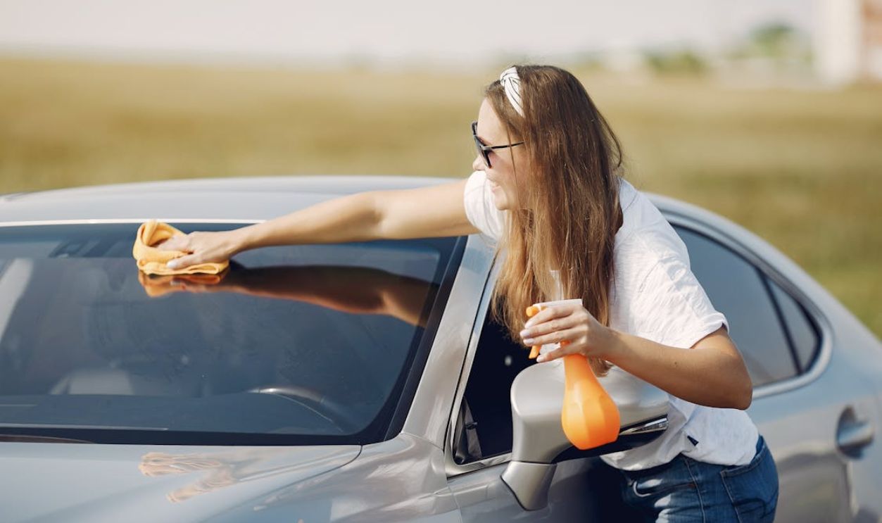Smiling young woman wiping automobile in countryside during car travel