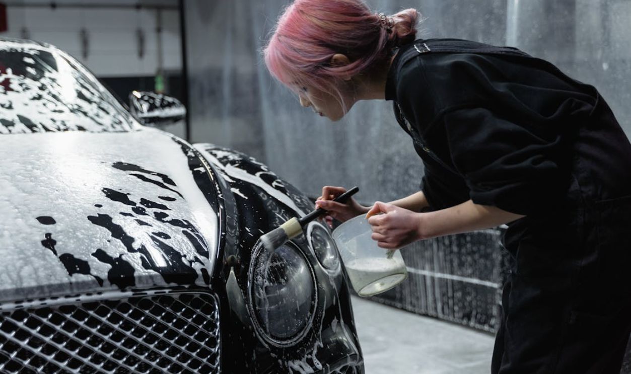 Photo of a Woman with Pink Hair Brushing the Headlight of a Black Car