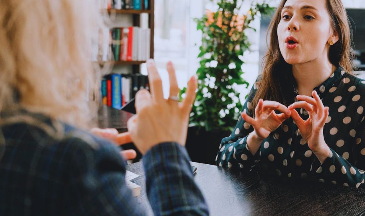 Young female friends communicating using sign language in library