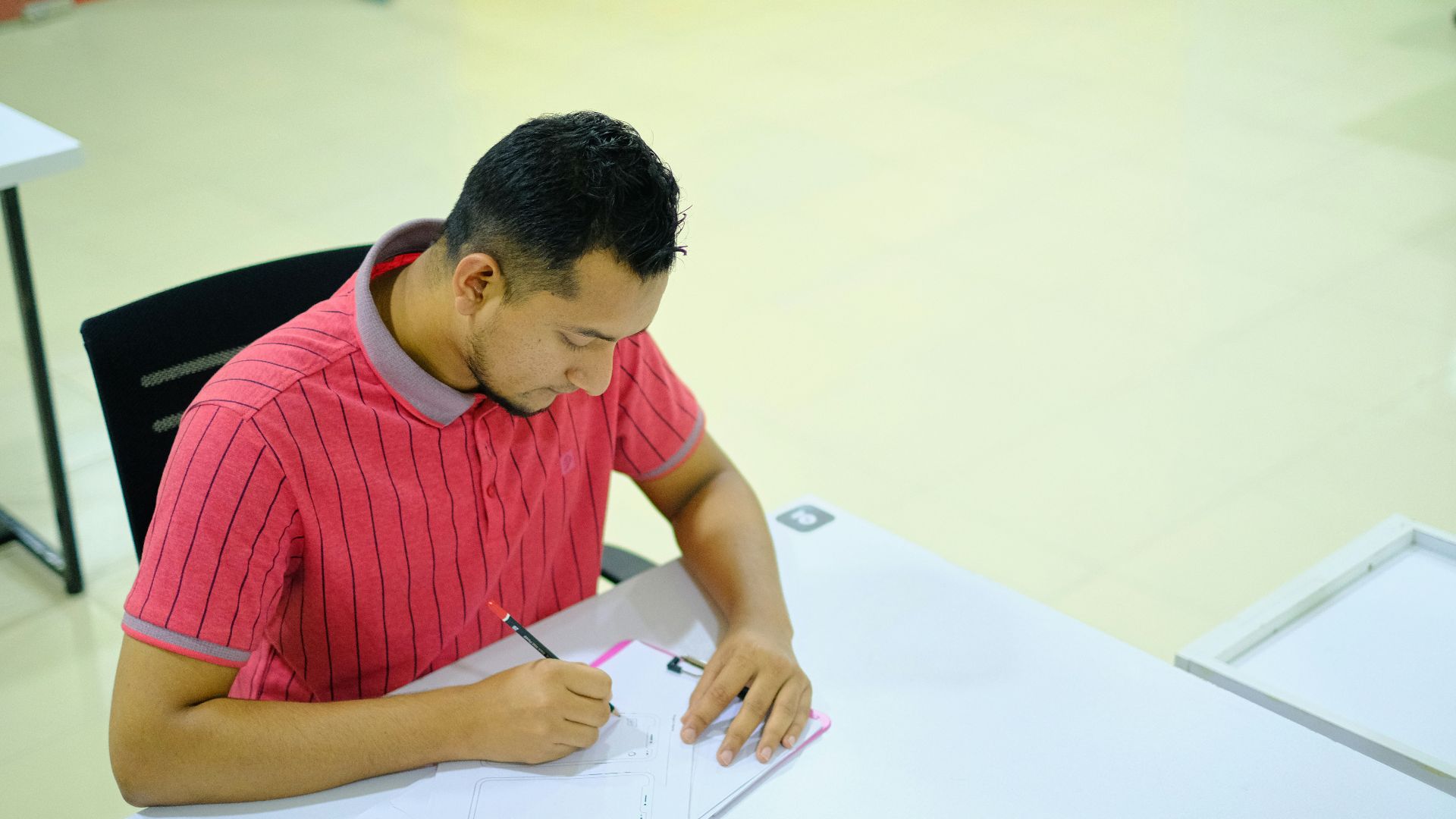 man in red and white striped crew neck t-shirt writing on white paper