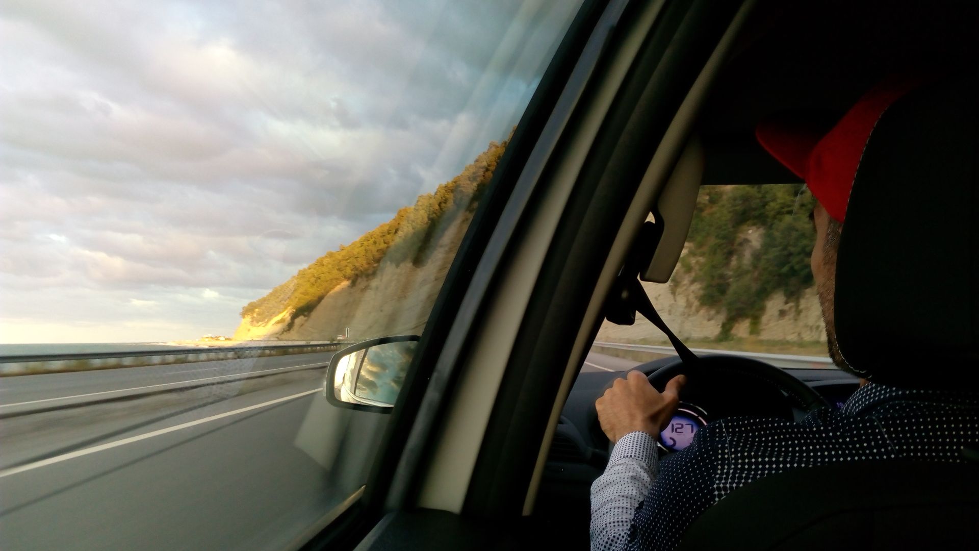 a shot from the backseat of a man in a red hat driving a car on the road