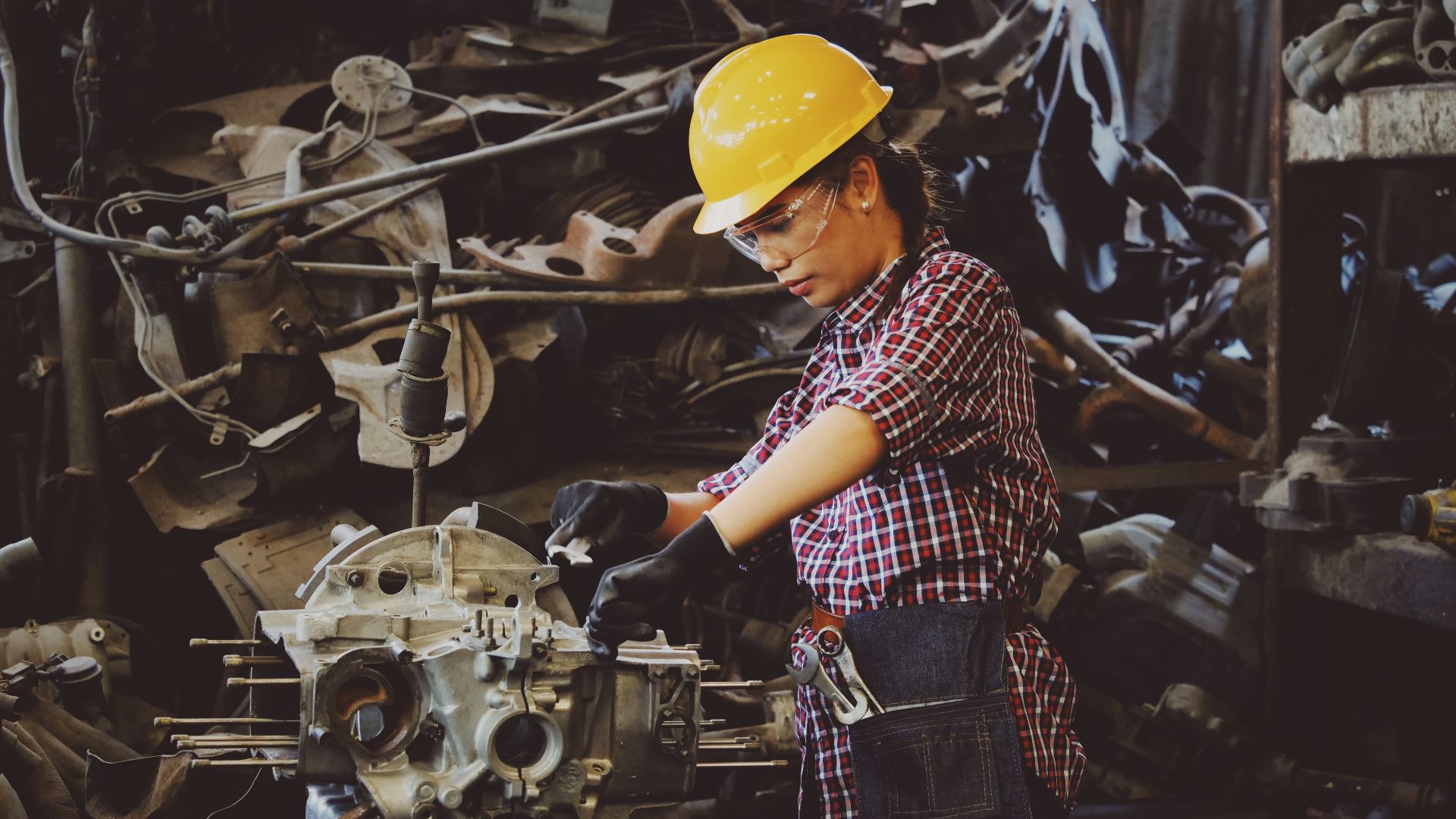 photograph of a woman mechanic in a yellow hard hat working on an engine